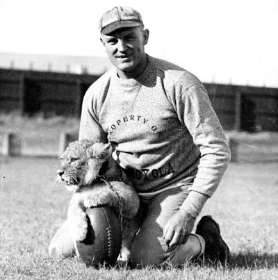 Football coach Tom Lieb next to a baby lion sitting on top of a football